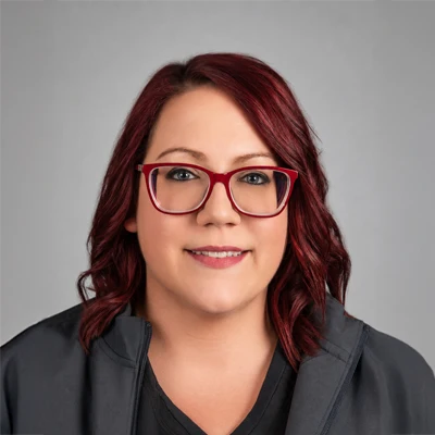 Staff member with shoulder length reddish brown hair and red glasses wearing a black blazer