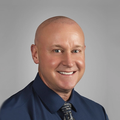Staff member with a shaved head wearing a navy blue shirt and patterned tie