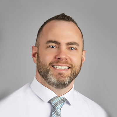 Staff member with short brown hair and a beard wearing a white shirt and patterned tie